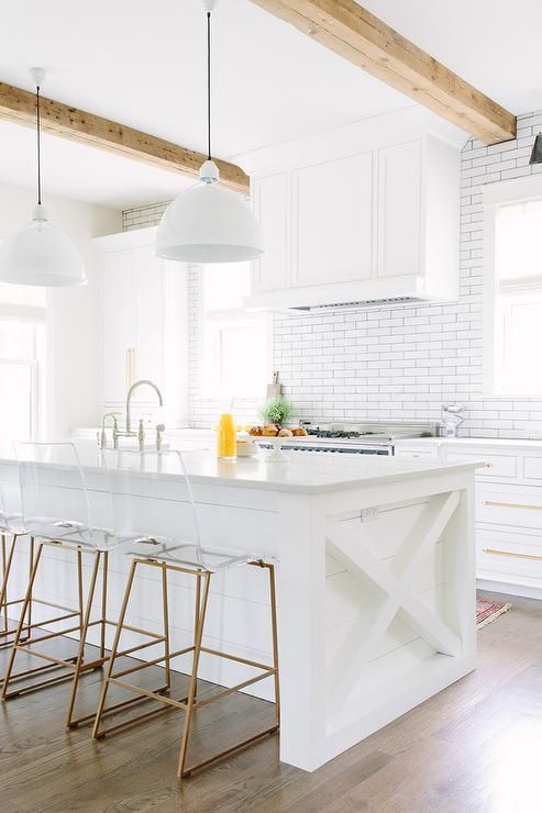 Brass and lucite counter stools are stat in front of a white .